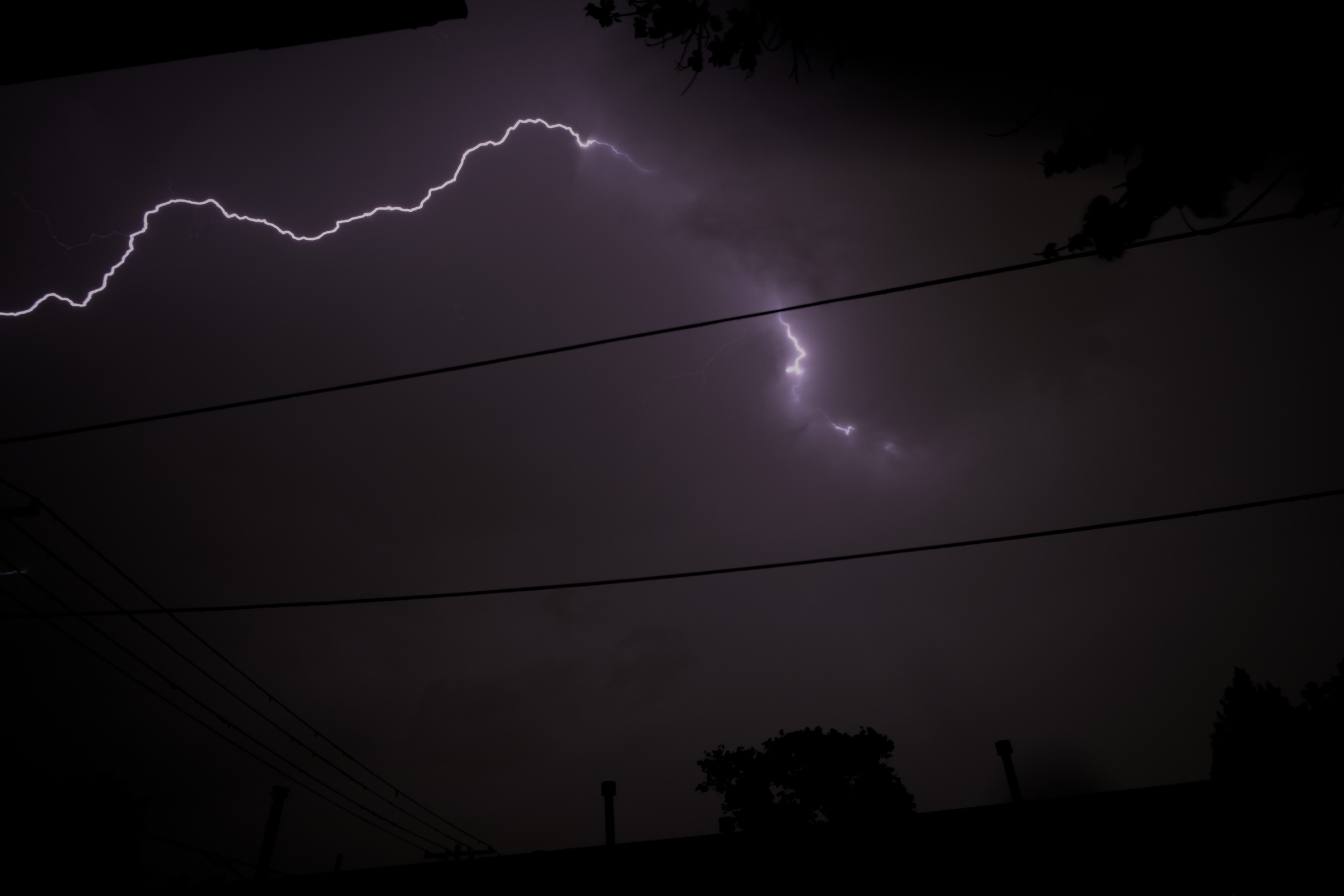 Lightning crossing a dark sky above power lines